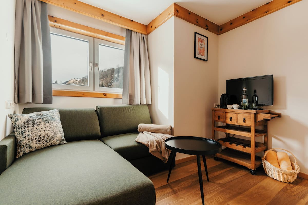 Una sala acogedora con un sofá seccional, un televisor, un mueble de madera y una ventana con cortinas.