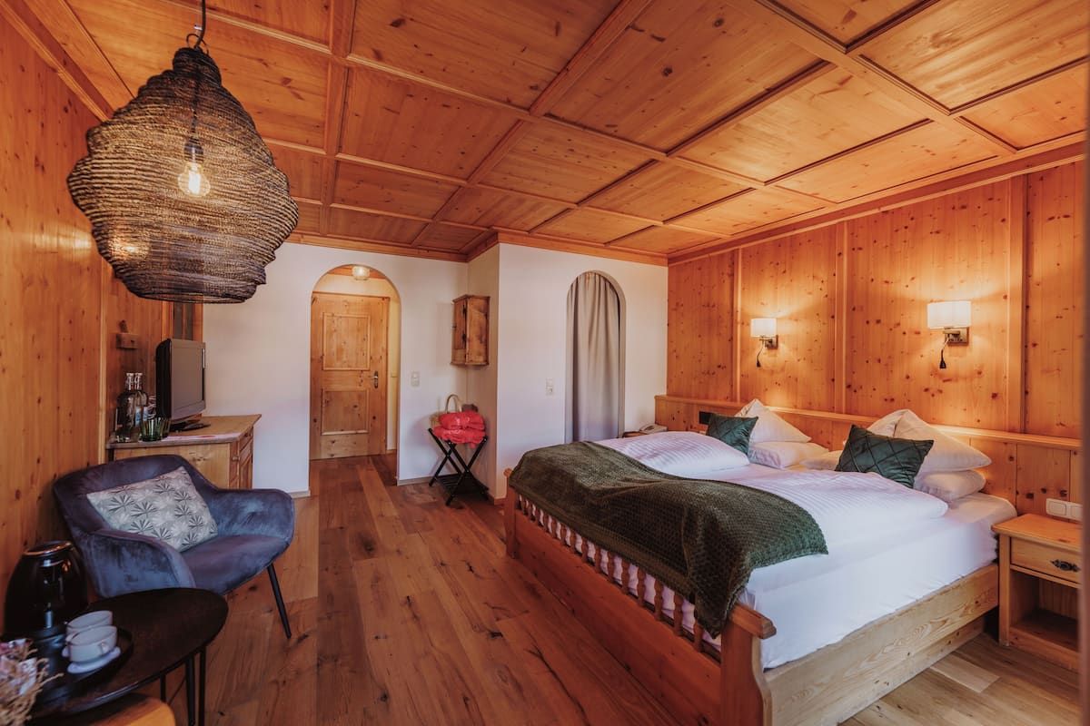 Una habitación con paneles de madera, una cama, una silla, una mesa y una lámpara colgante.