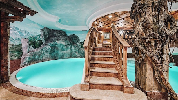 Ein Poolbereich mit einer Holztreppe, die zu einer Terrasse führt, umgeben von einem Wandbild von Bergen und einem Baumstamm.