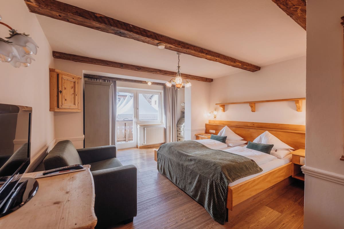 Un dormitorio con cama y mesita de noche de madera, televisión y un área de estar con mesa y sillas.