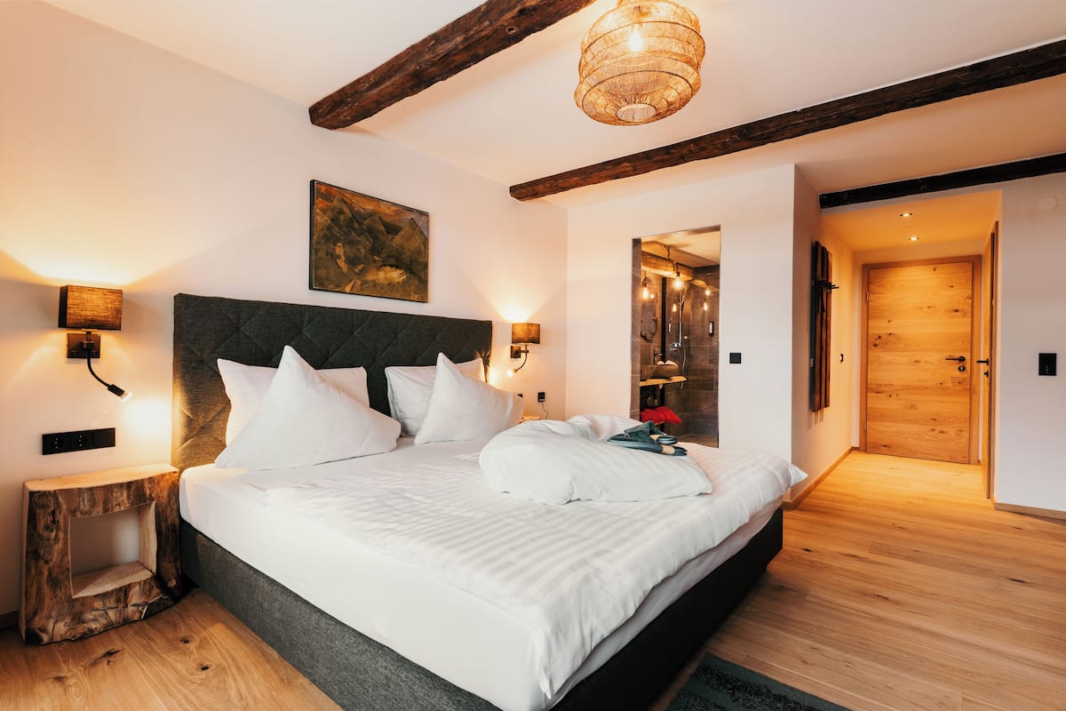 Un dormitorio moderno con una cama grande, vigas de madera, una lámpara colgante y una puerta de madera.
