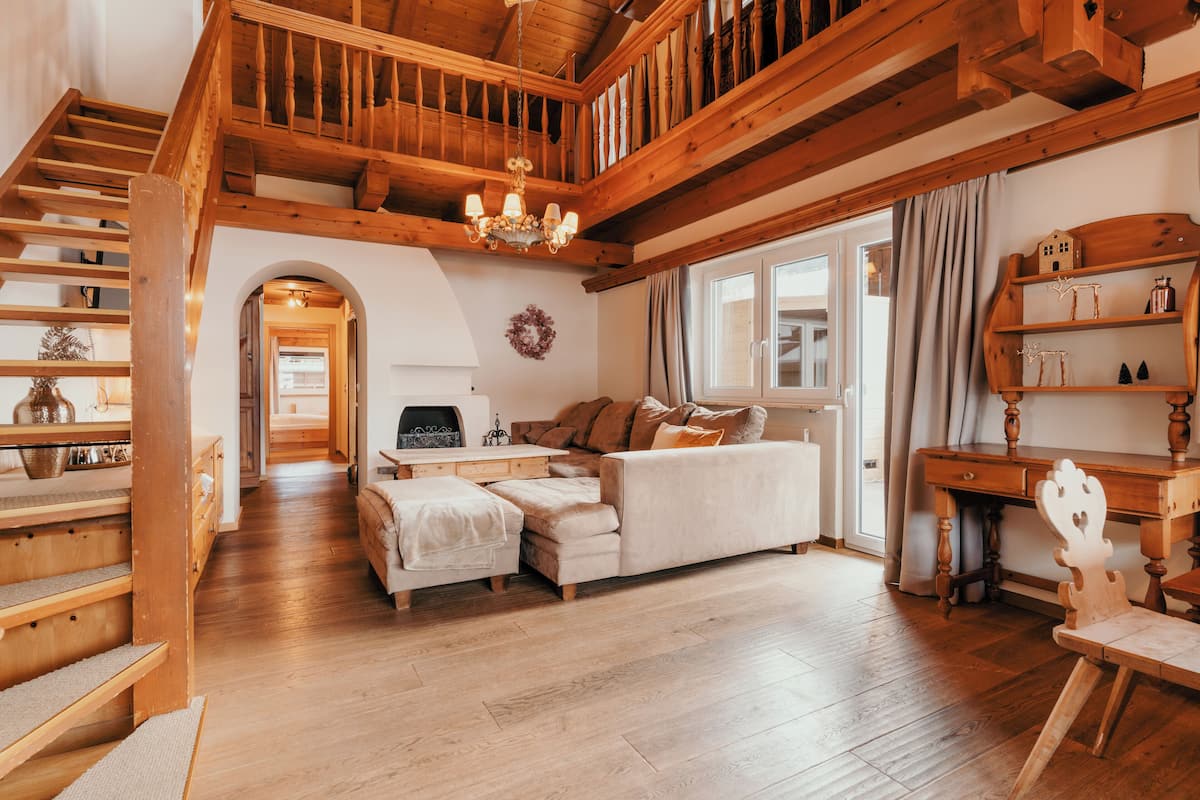 Un amplio salón con una escalera de madera, un sofá blanco y un escritorio de madera.