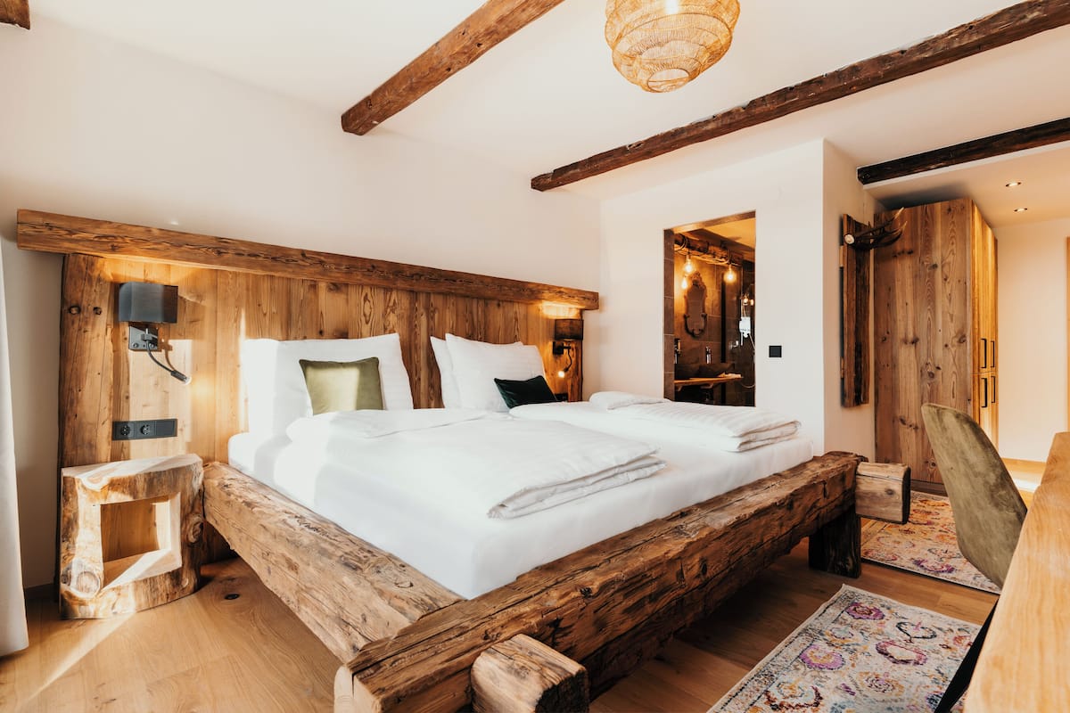 Una cama con estructura de madera y sábanas blancas, una mesita de noche de madera y una lámpara de techo tejida.