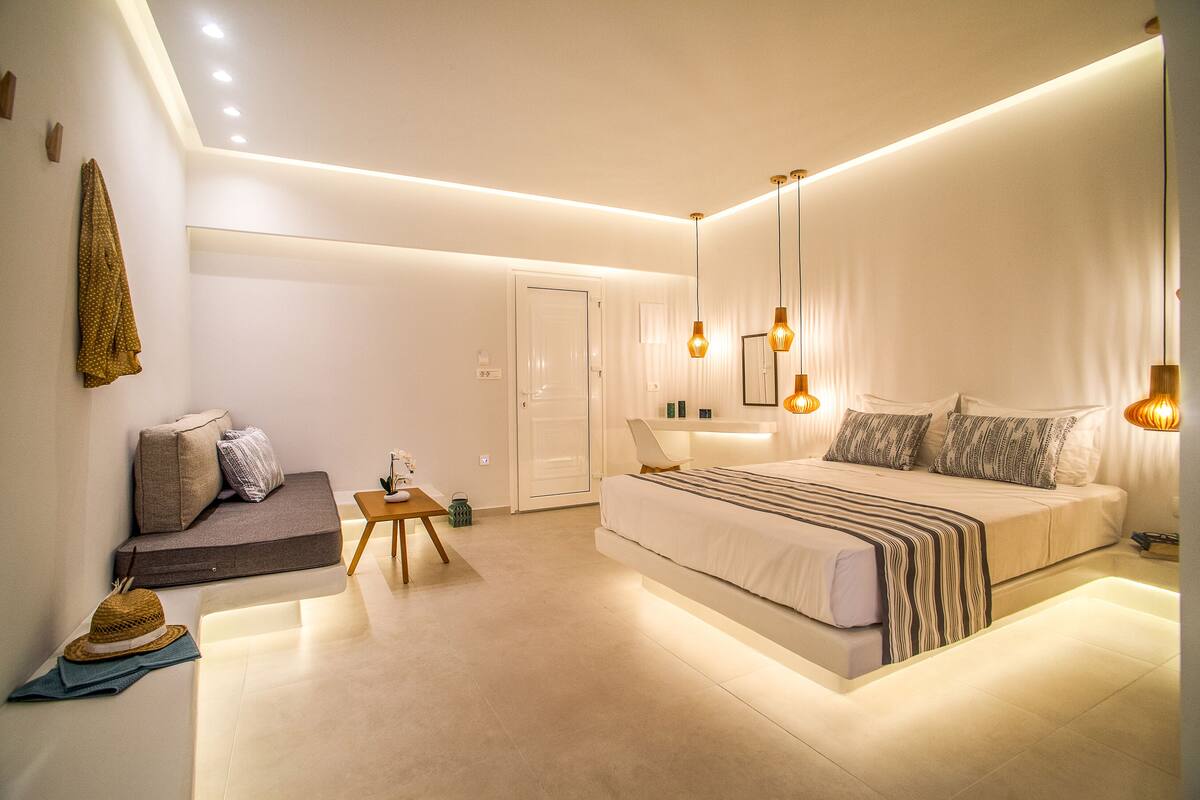 A modern bedroom with a large bed, bedside tables, a sofa, and a small table with a hat and scarf.