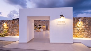 A modern entrance with a stone wall and a sign reading "MARGARENIA". - Margarenia (Santorini)