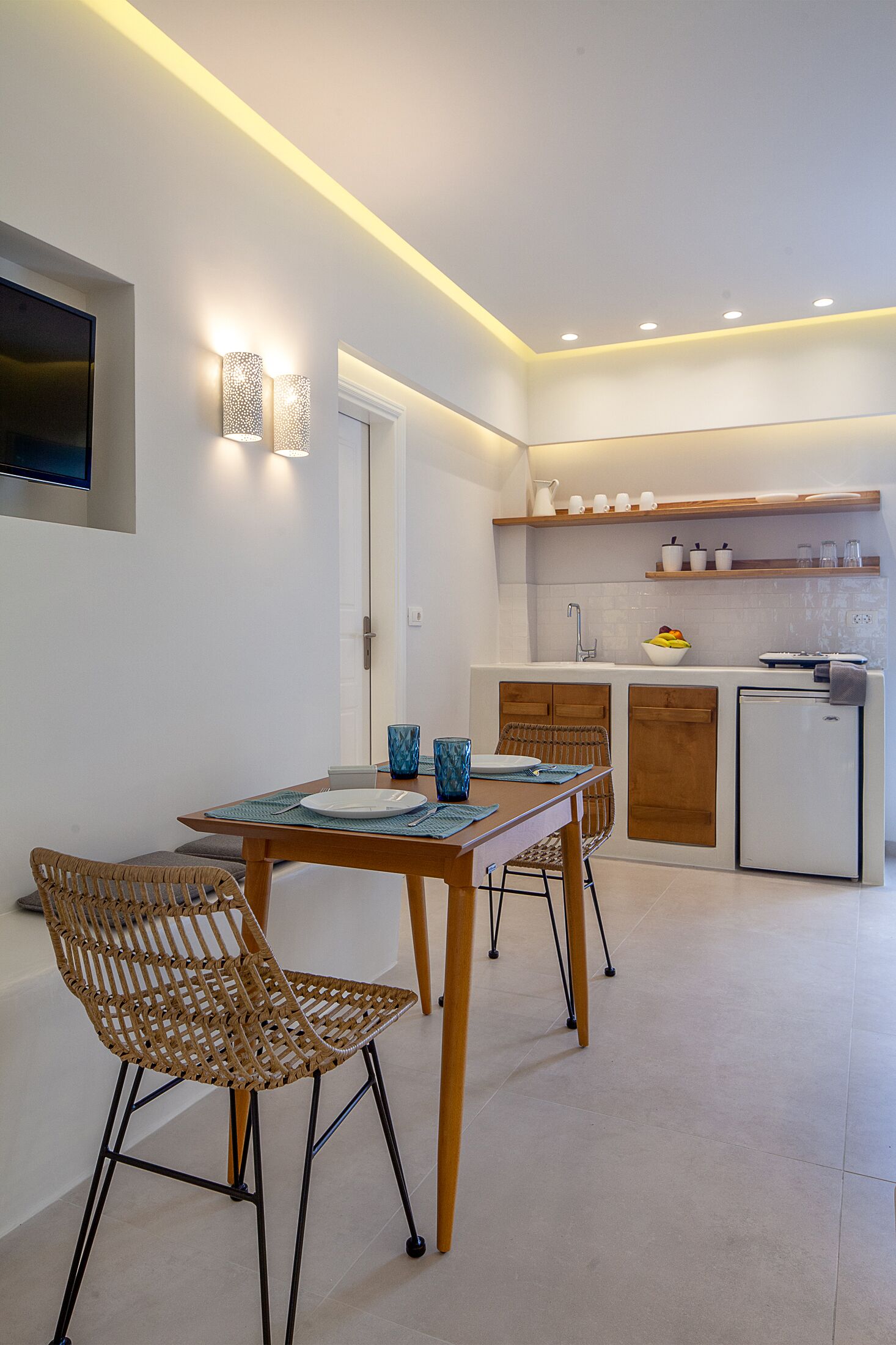A modern kitchen with a dining area, featuring a table with chairs, a built-in oven, and a small refrigerator.