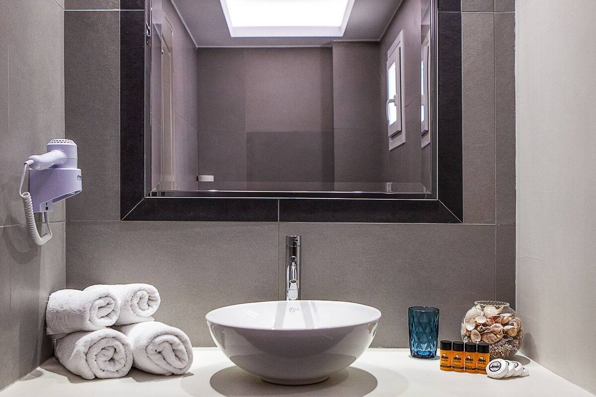 A modern bathroom with a large mirror, a white sink, and a towel rack.