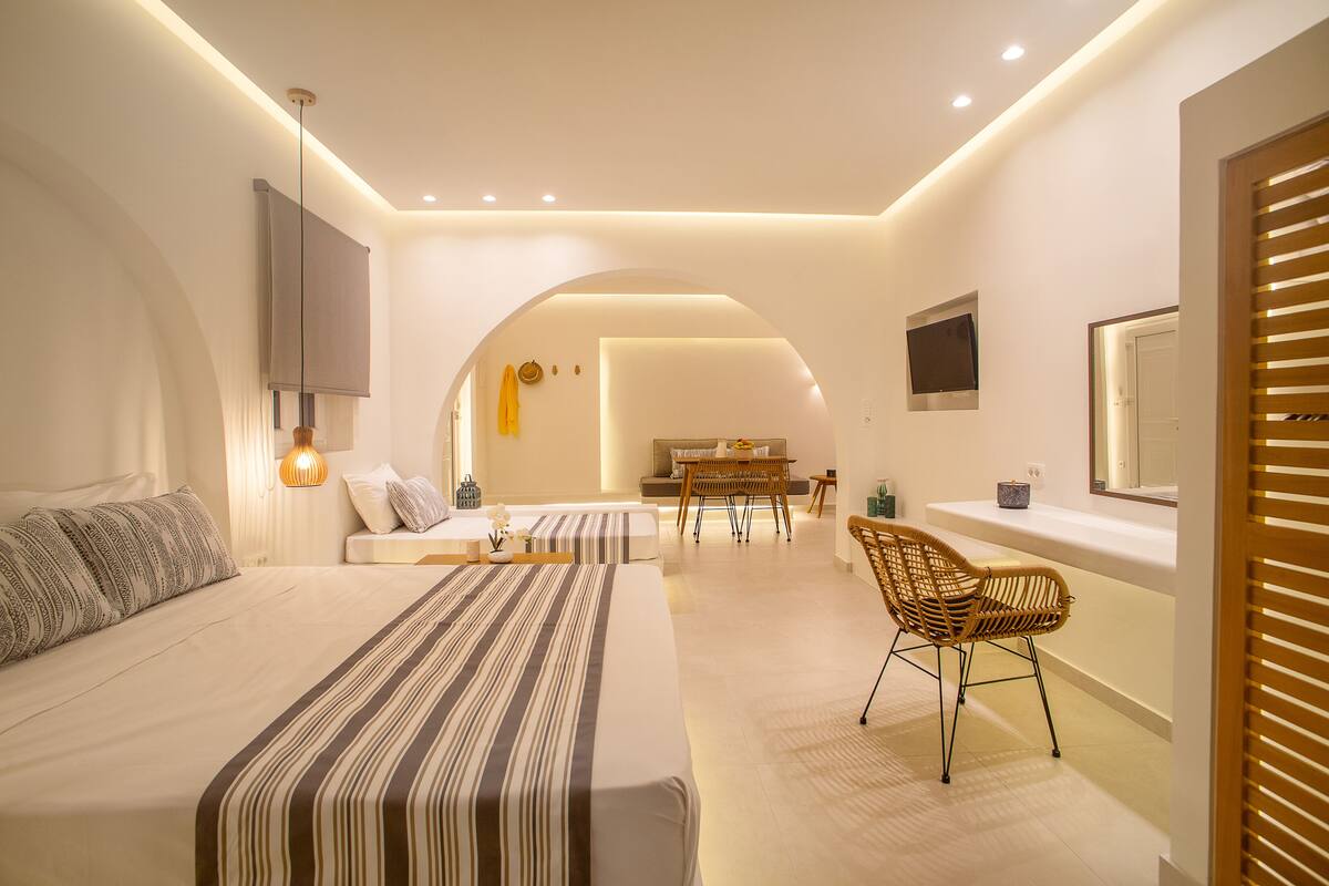 A modern hotel room with a large bed, a seating area with a table, and a TV mounted on the wall.