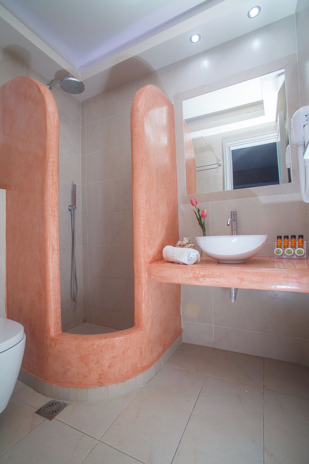 A modern bathroom with a large, curved shower enclosure, a white sink with a vessel basin, and a mirror above the sink.