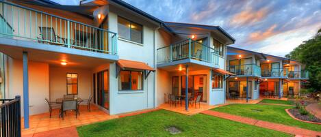 A modern multi-story hotel with balconies, outdoor seating areas, and a well-maintained lawn.