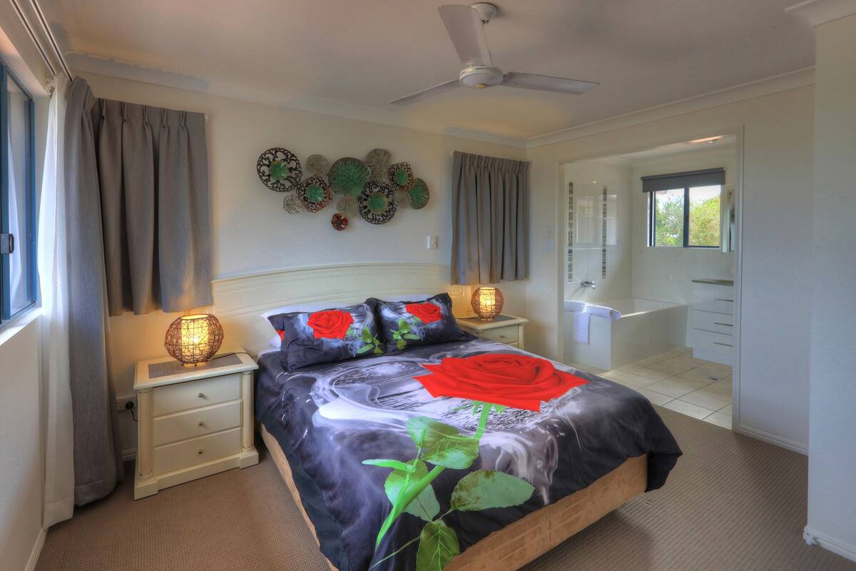 A bedroom with a bed, nightstands, a ceiling fan, and a bathroom visible through an open door.