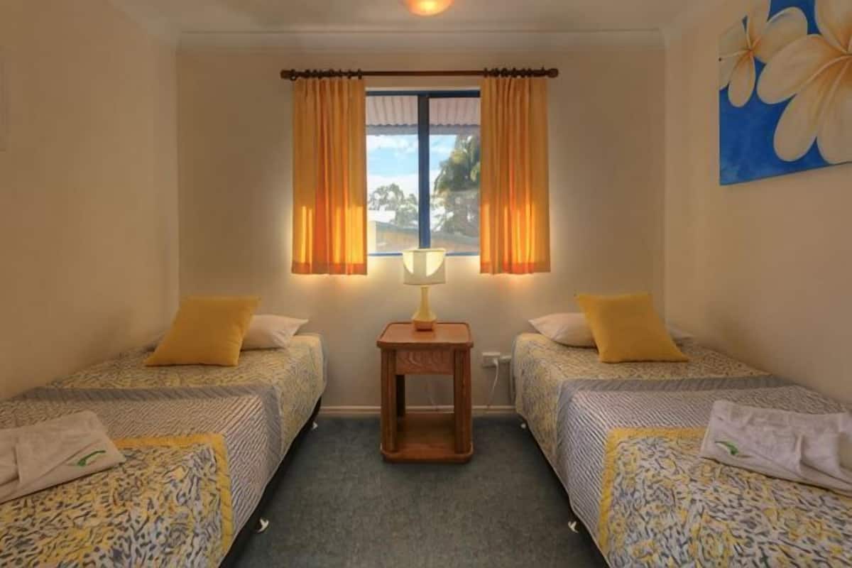 Una habitación con dos camas, una mesita y una ventana con cortinas.