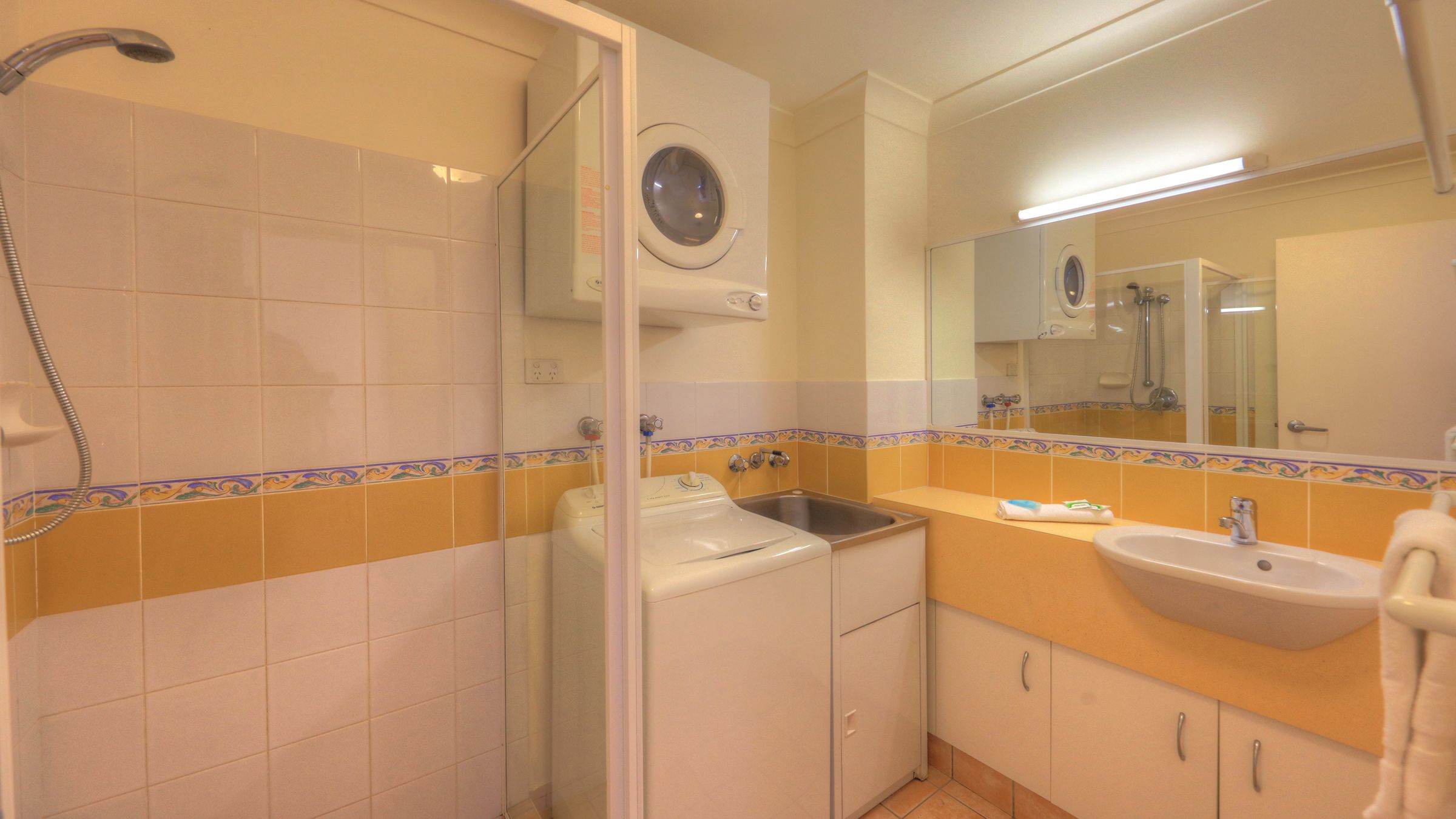 Un baño con lavadora, lavamanos, espejo y ducha.
