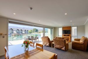 Uma sala de estar ampla com uma grande janela com vista para uma piscina e montanhas, uma mesa de jantar de madeira e assentos confortáveis.