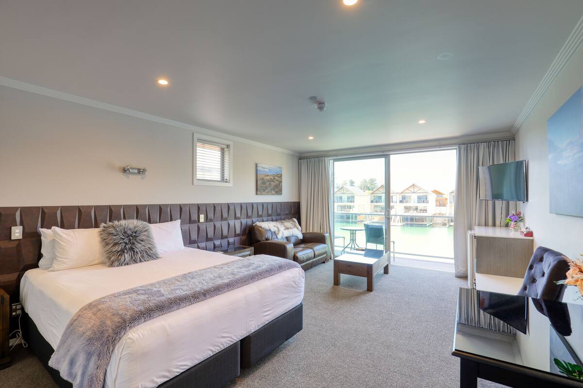 A hotel room with a large bed, a sofa, a small table, and a TV.