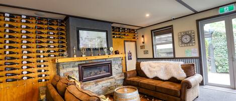 A cozy lounge area with leather sofas, a stone fireplace, and a wall of wine bottles.