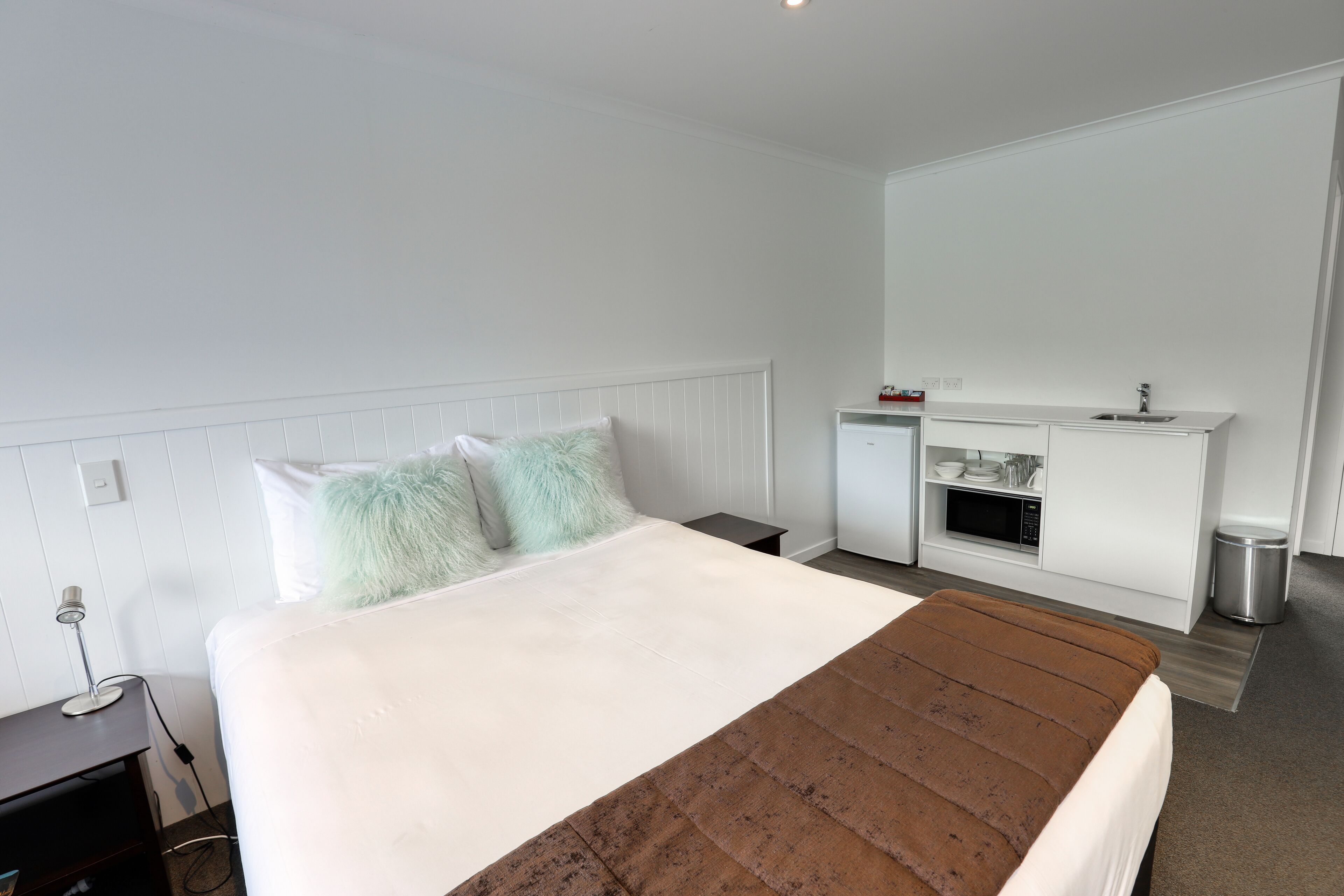 Una habitación de hotel moderna con una cama grande, una kitchenette pequeña y una decoración en tonos blancos.