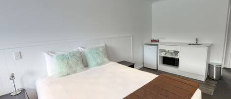 Una habitación de hotel moderna con una cama grande, una kitchenette pequeña y una decoración en tonos blancos.
