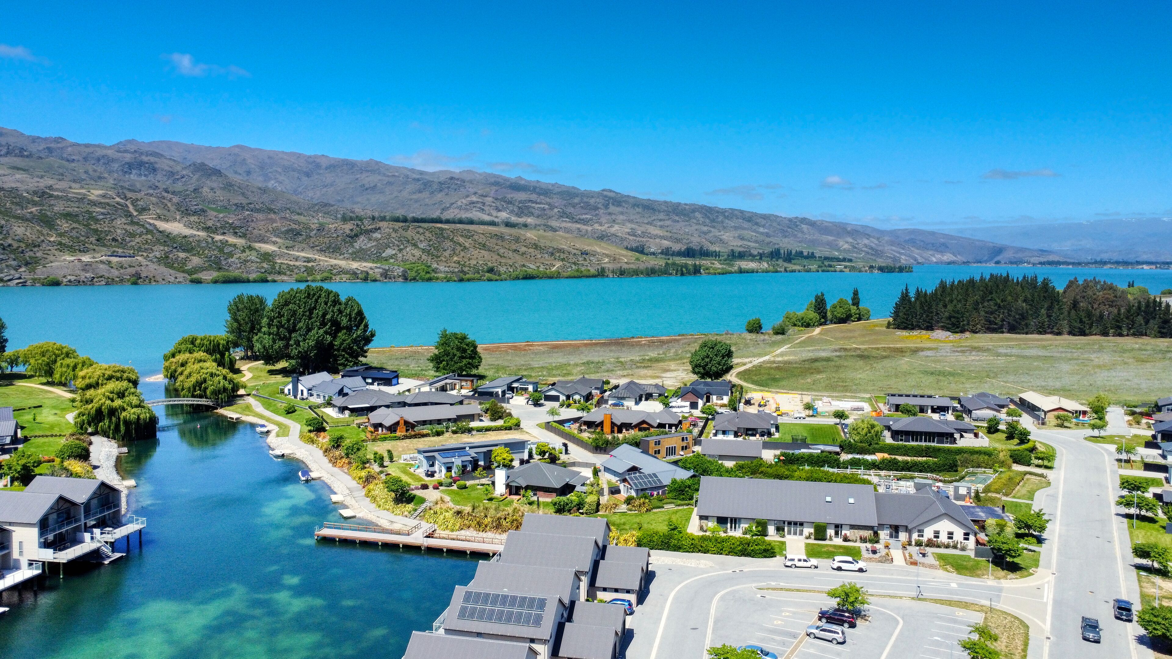 A lakeside residential area with houses, a dock, and a clear view of the lake and mountains.