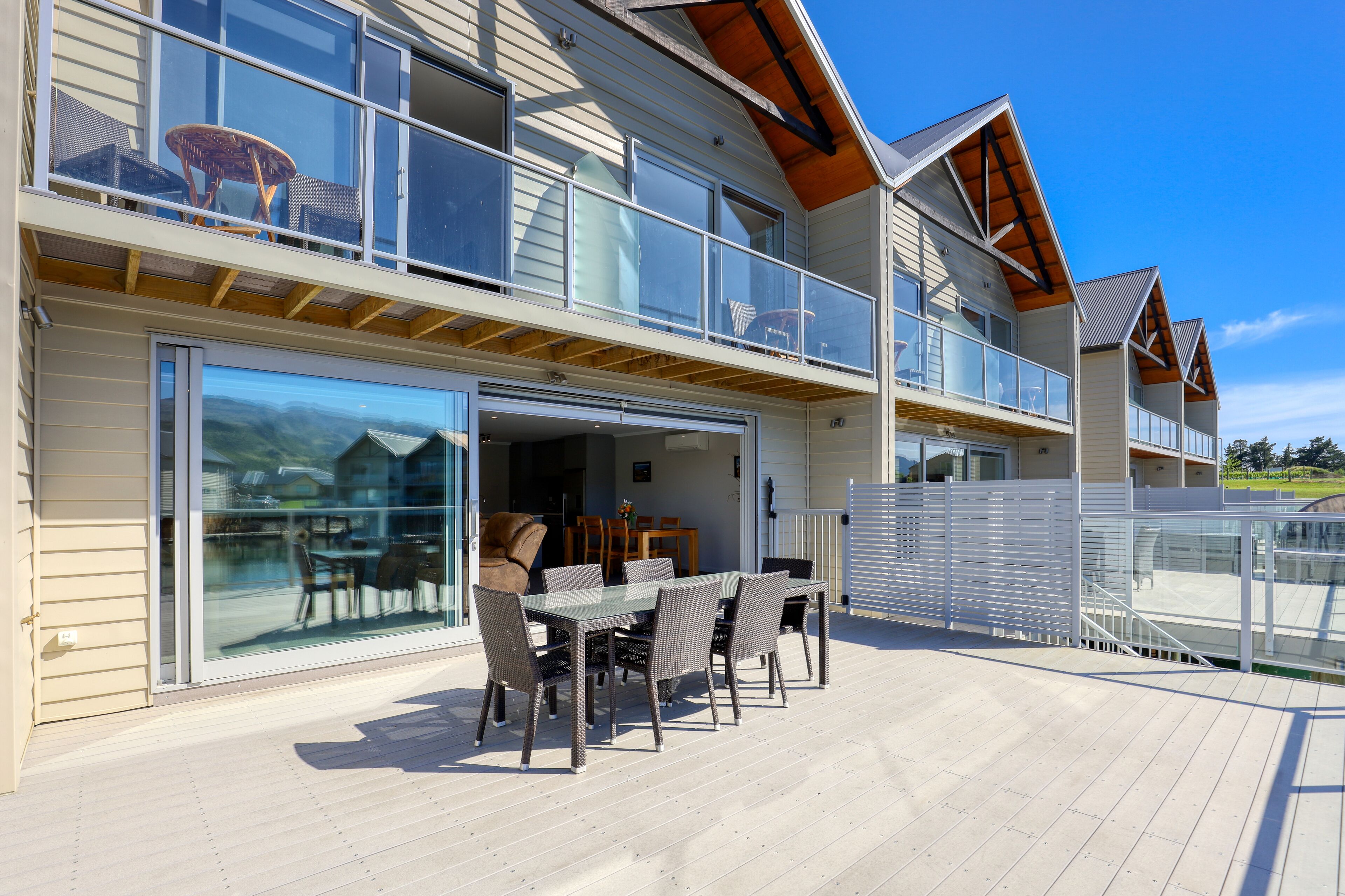 A modern two-story house with a balcony, a dining area with a table and chairs, and a garage door.