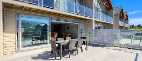 A modern two-story house with a balcony, a dining area with a table and chairs, and a garage door.