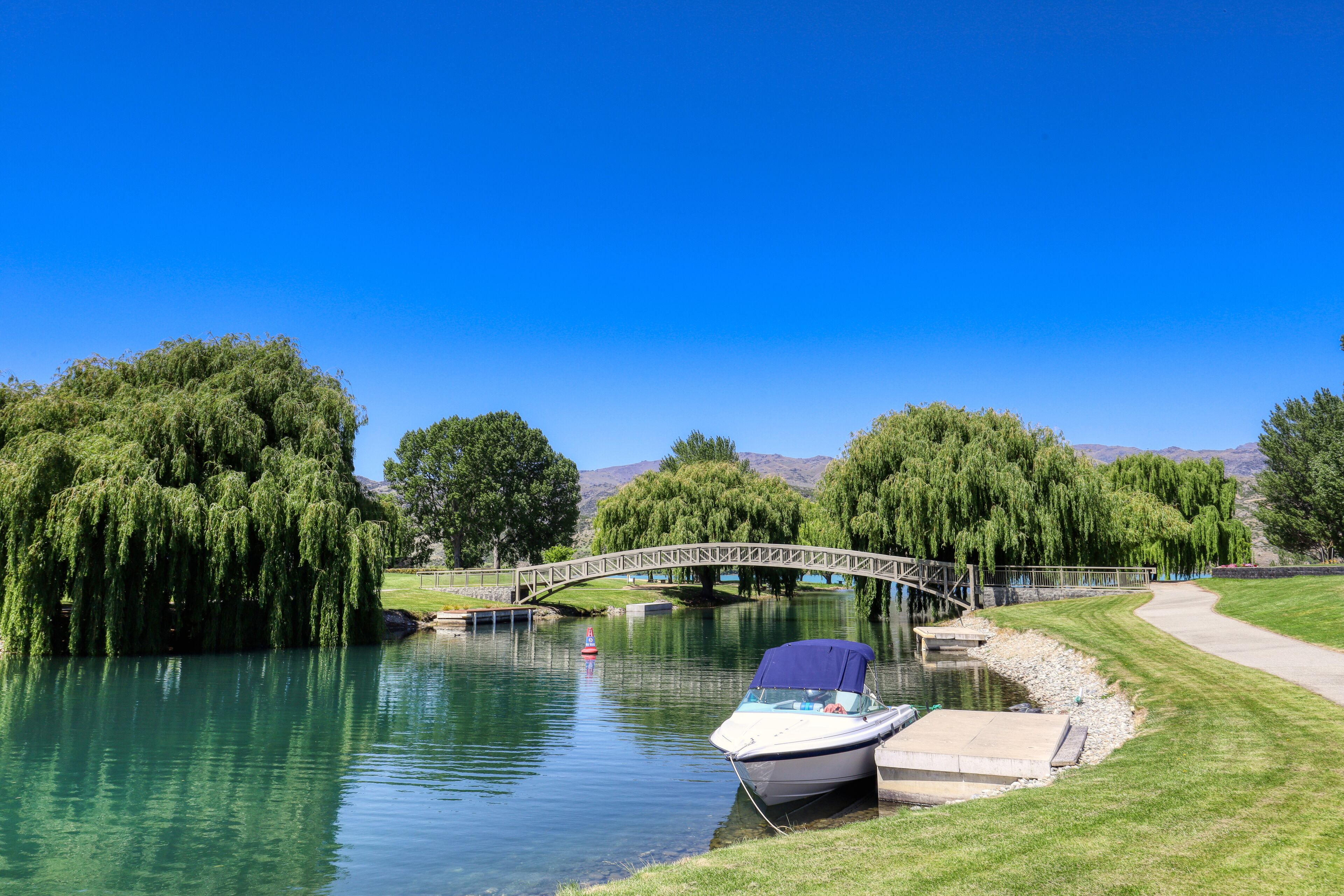 A boat docked near a grassy area with a bridge in the background.