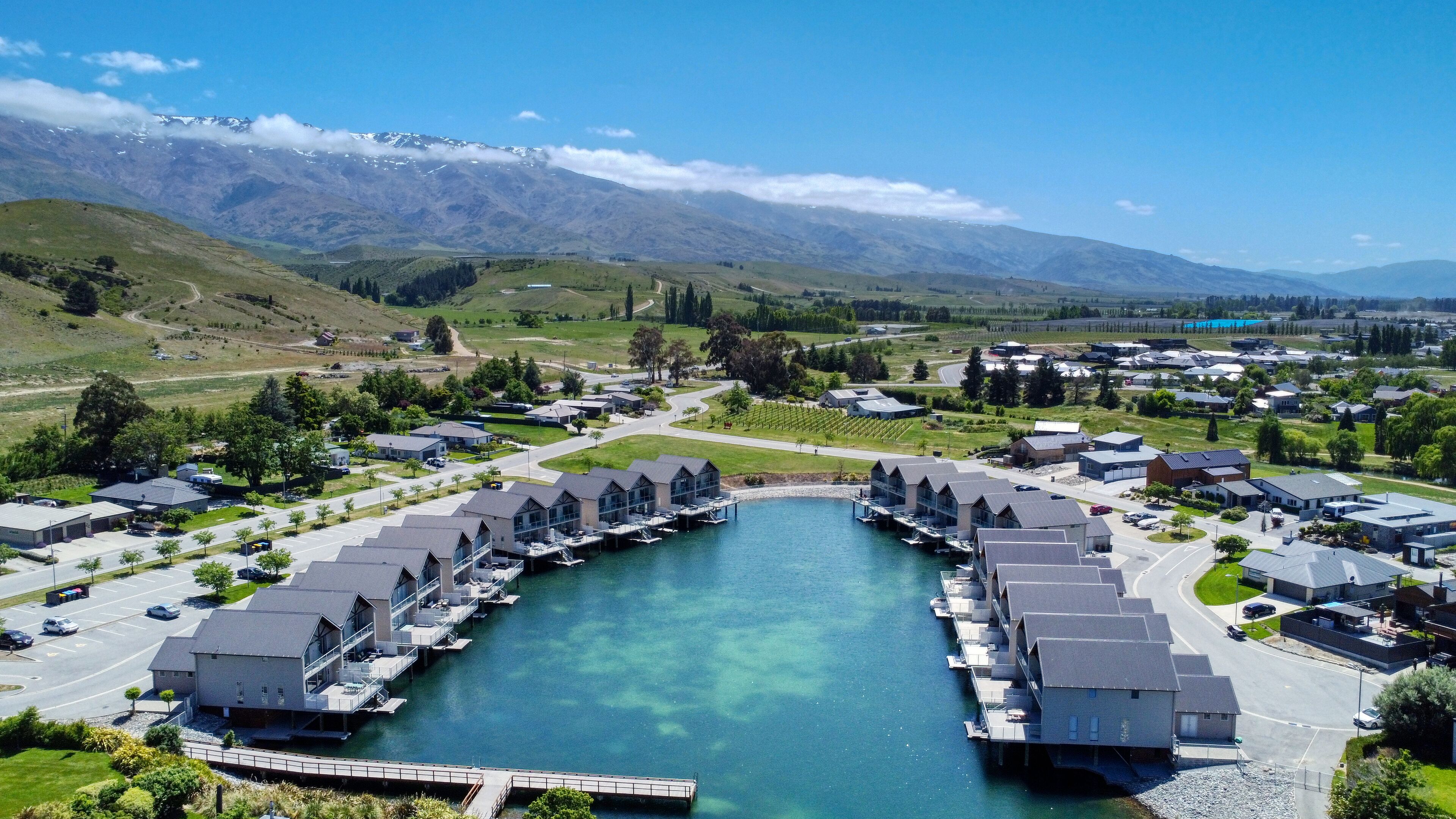 A lakeside hotel with multiple buildings connected by walkways over the water, surrounded by a mountainous landscape.