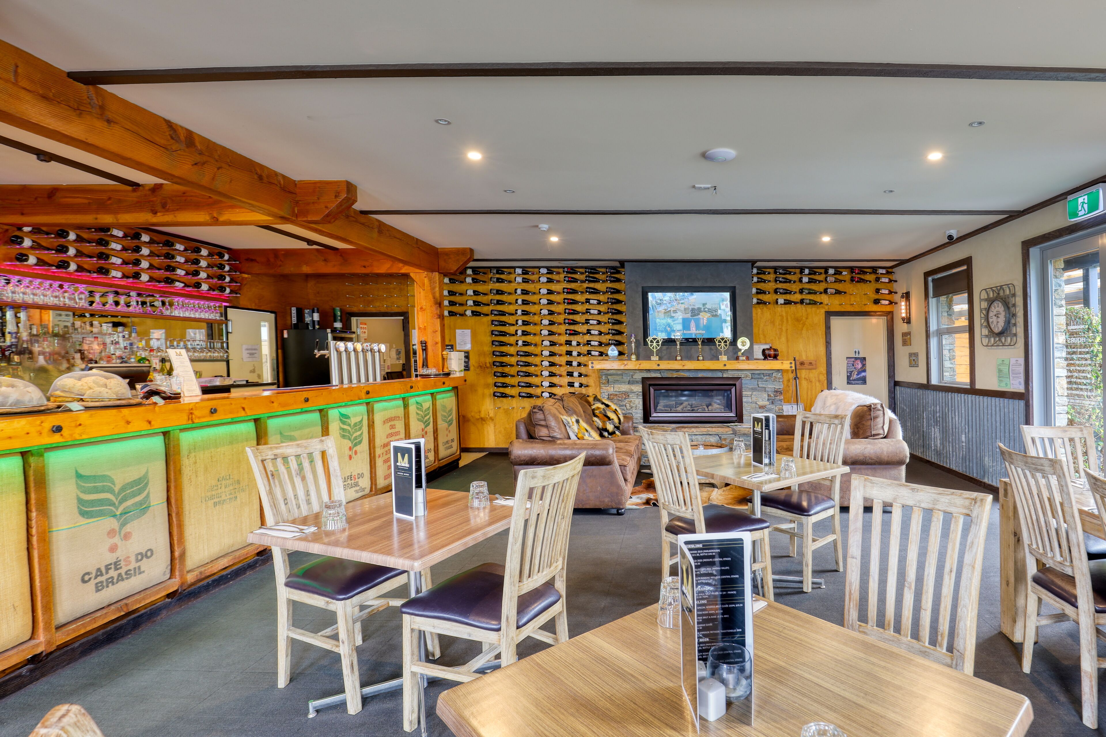 Un restaurante con mobiliario de madera, una zona de bar con botellas de vino y una chimenea.
