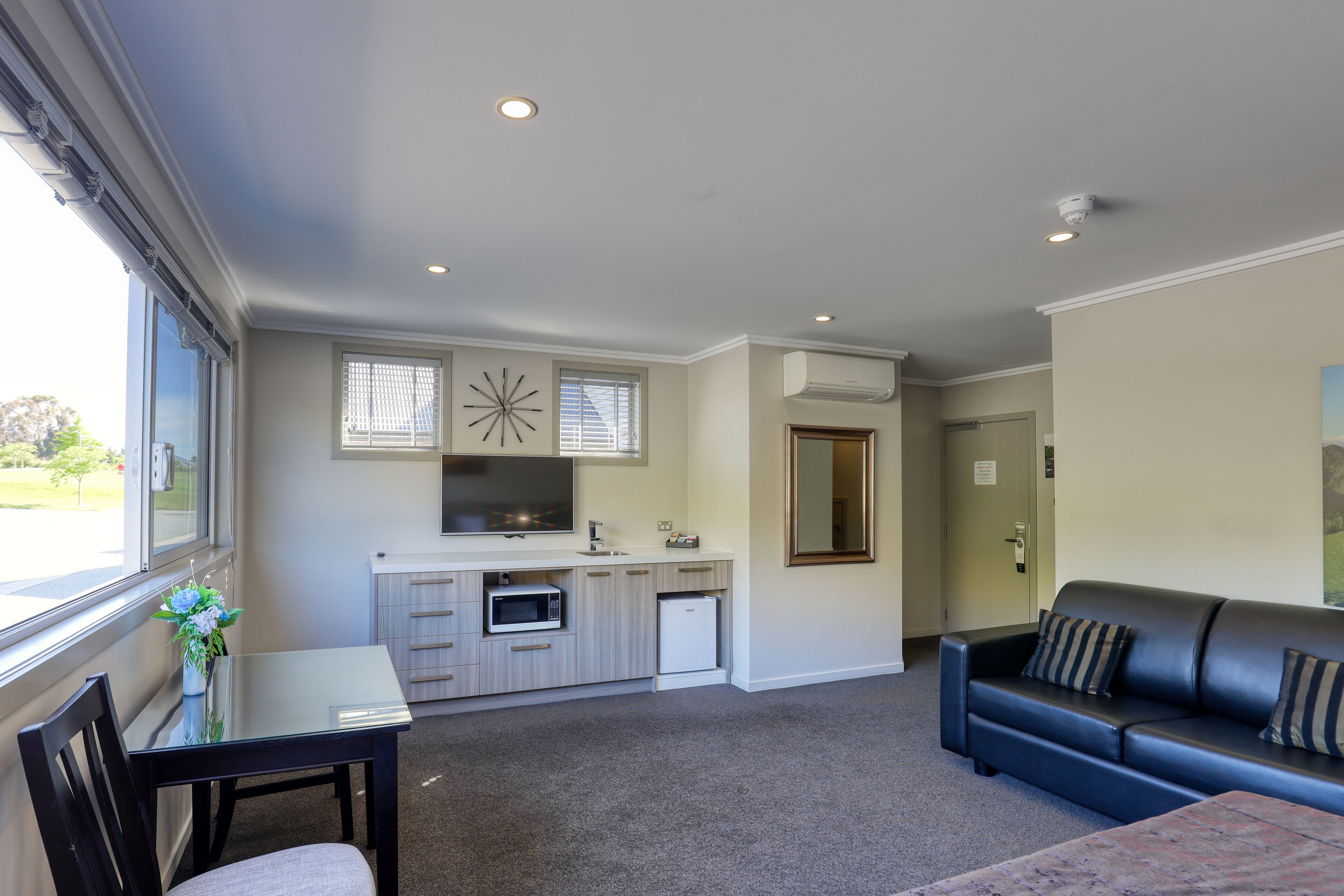 A modern kitchen with a built-in microwave and oven, a dining area with a table and chairs, and a living room with a sofa and a large window.