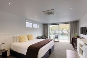 Habitación de hotel con una cama grande, un escritorio, una silla, un televisor y vistas a un cuerpo de agua y edificios.