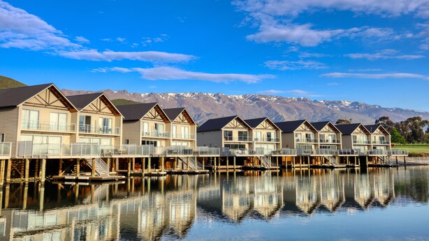 A row of waterfront cottages with balconies, wooden decks, and a mountain backdrop. - Lake Resort by Marsden (Mount Pisa)