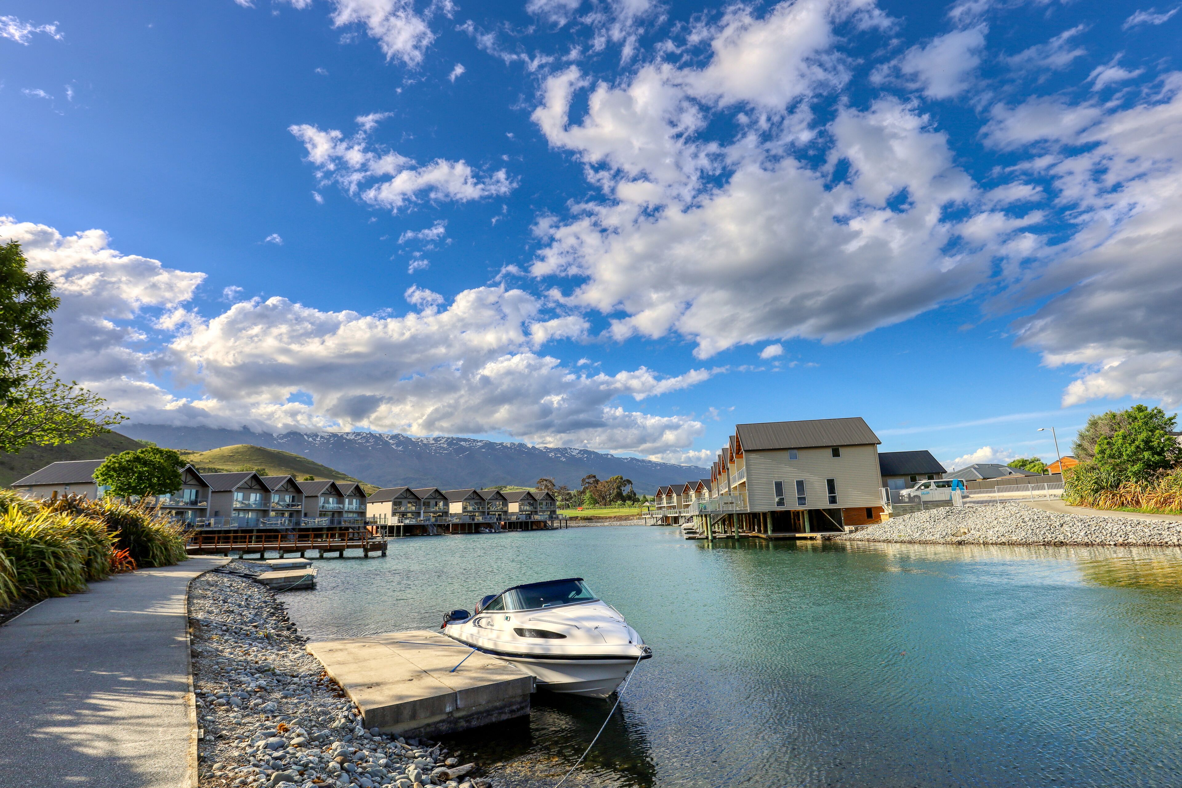 A waterfront property with a dock, a boat, and a row of houses with a mountain backdrop.