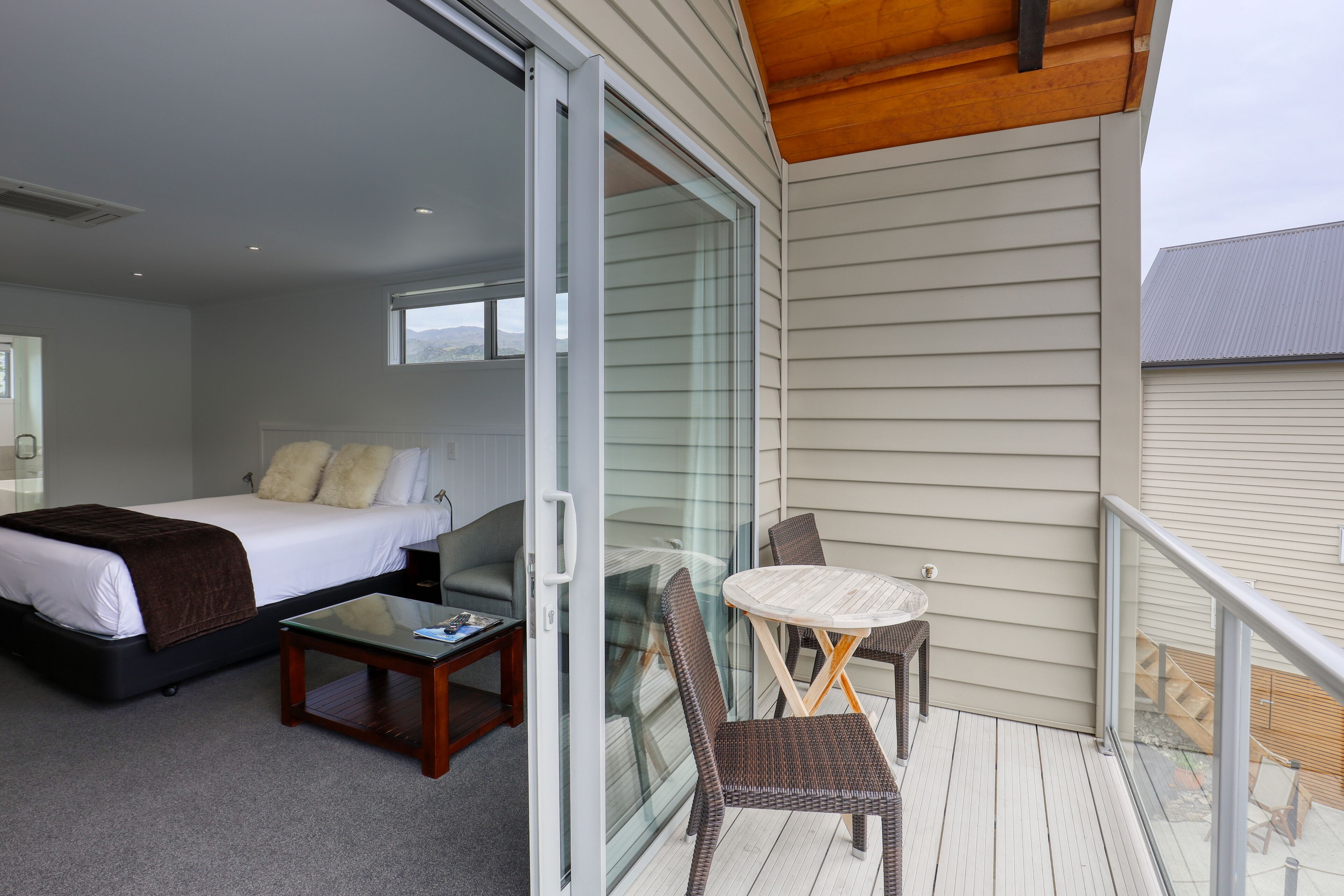 A hotel room with a bed, a small table, a chair, and a balcony with a table and chairs.