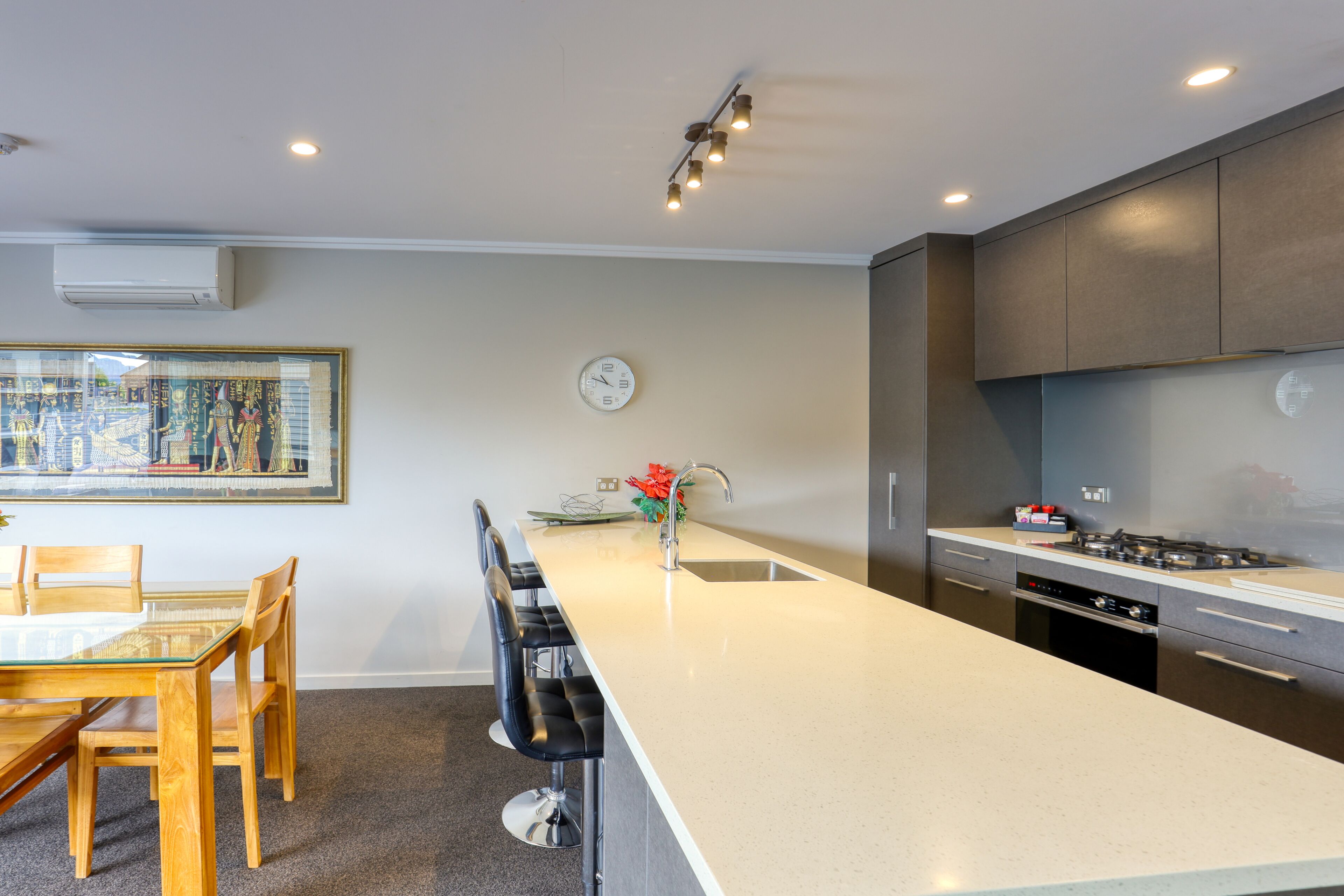 A modern kitchen with a central island, a dining area with a glass table, and a painting on the wall.