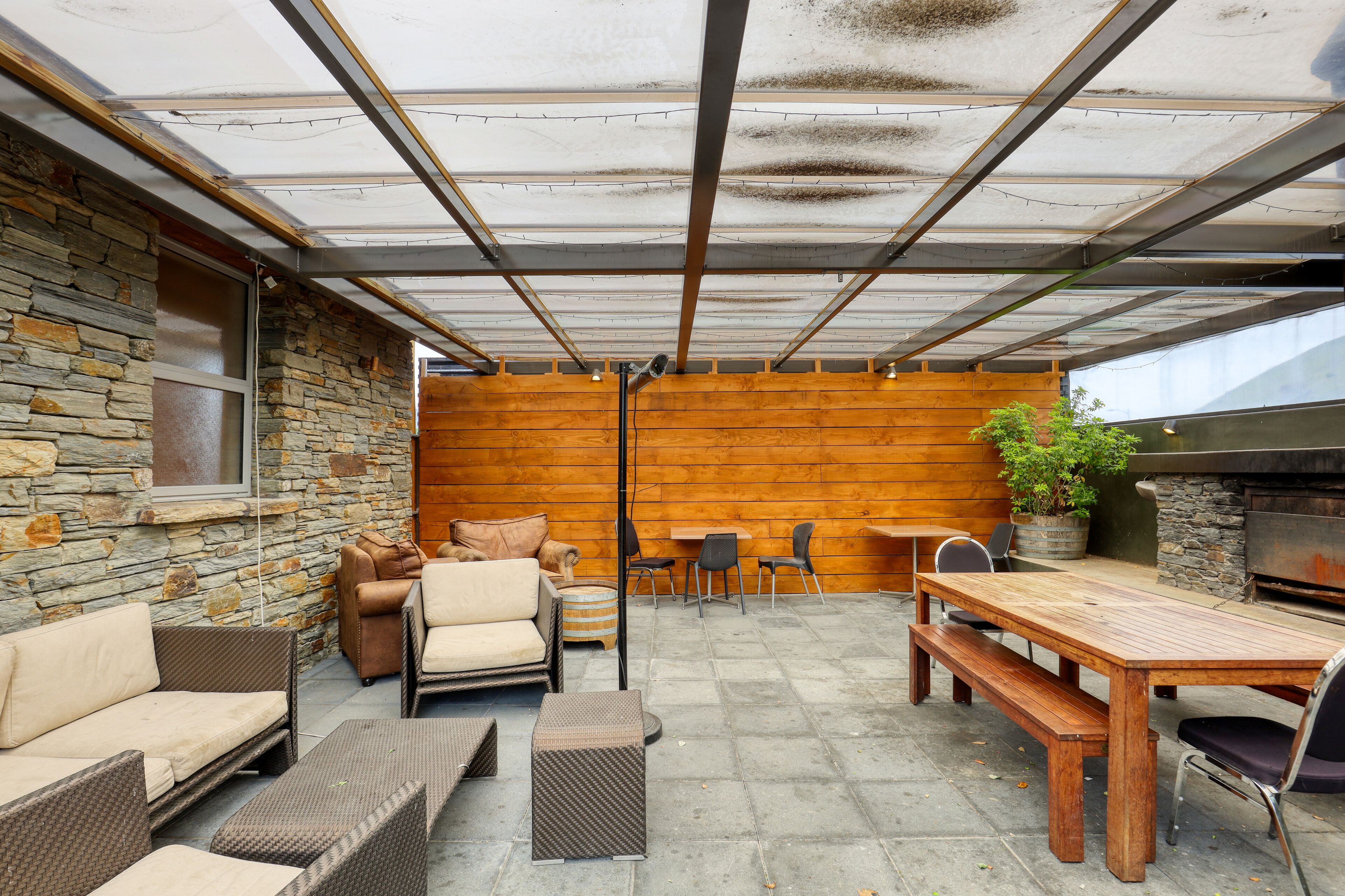 En udendørs patio med stenvægge, træmøbler og grillområde.