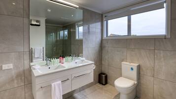 Un bagno moderno con un ampio specchio, doppio lavabo, WC e finestra che lascia entrare luce naturale.