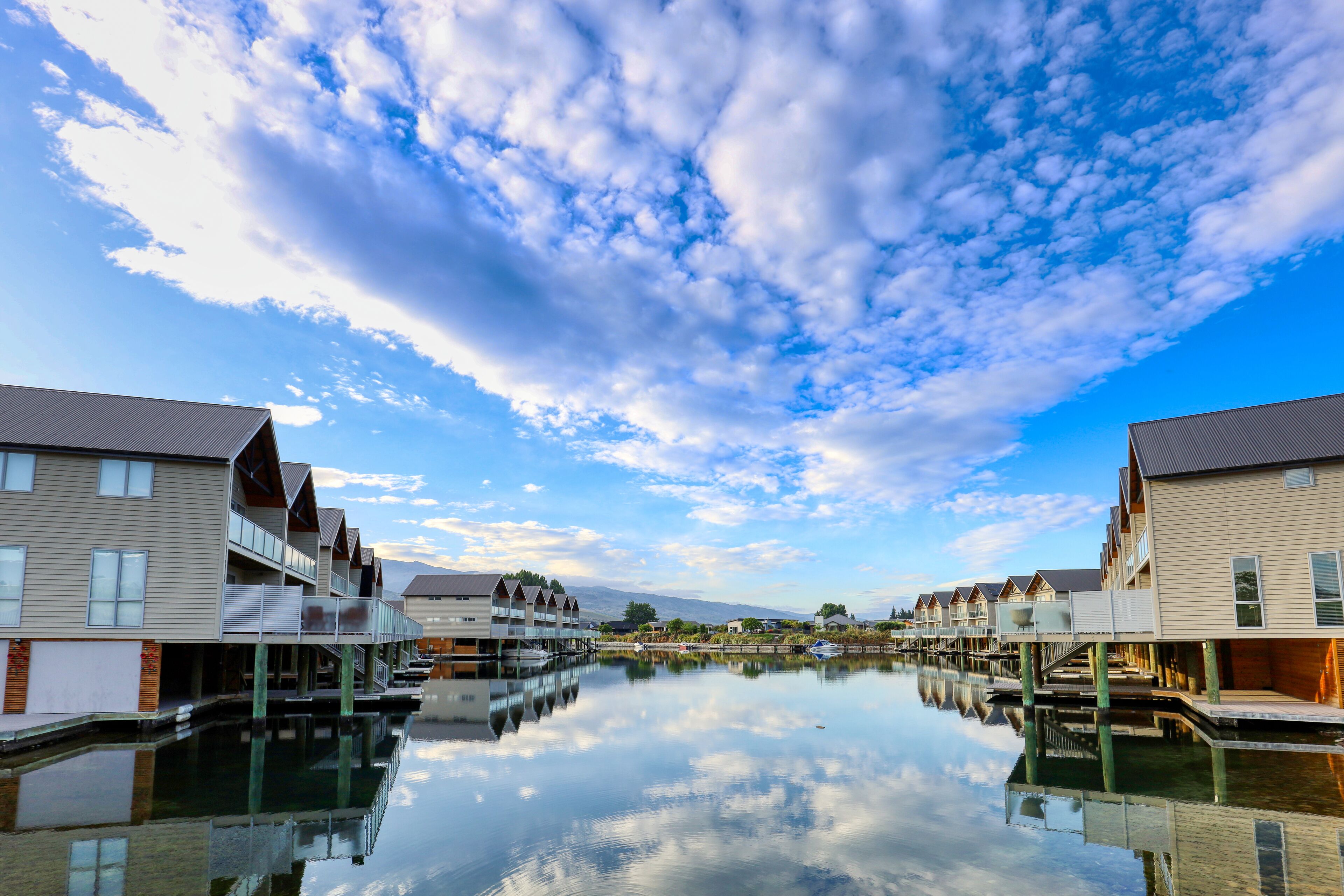 Un hotel frente al mar con varias edificaciones conectadas por pasarelas sobre el agua, que refleja el cielo y las nubes.
