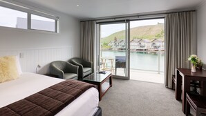 A hotel room with a large bed, two chairs, a small table, and a view of a water body and buildings. - Lake Resort by Marsden (Mount Pisa)