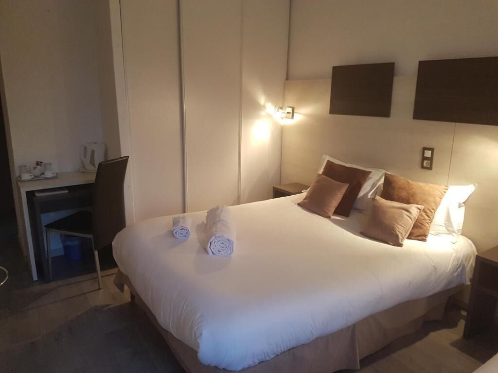 A hotel room with a large bed, bedside tables, a desk, and a wall-mounted light.