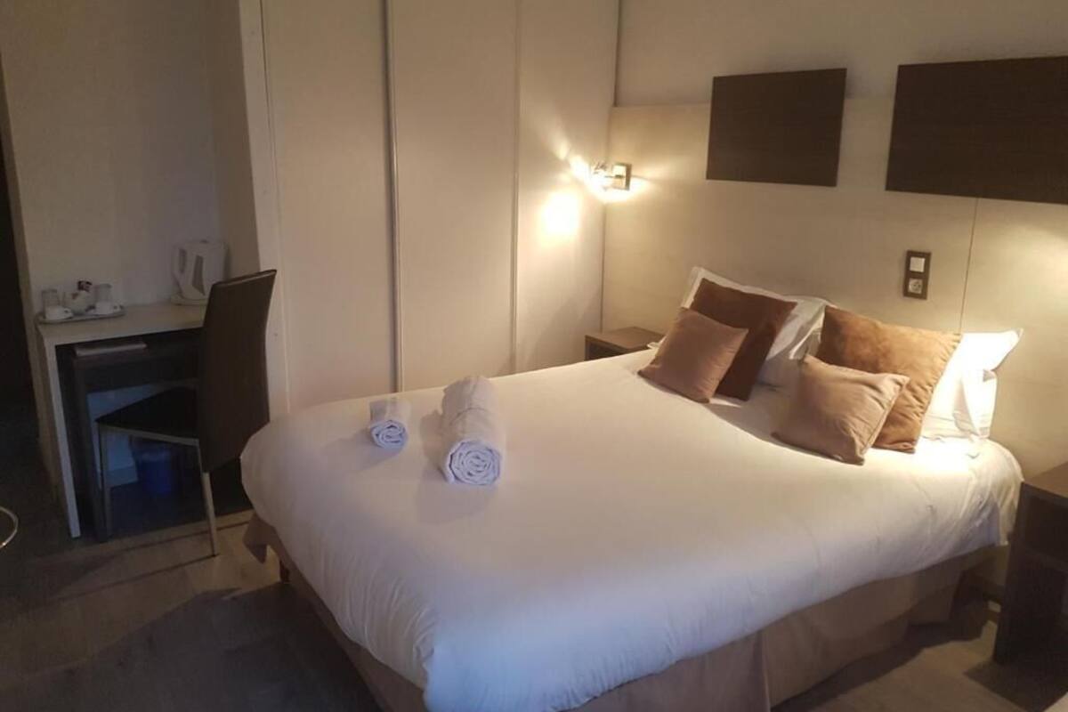 A hotel room with a large bed, bedside tables, a desk, and a wall-mounted light.