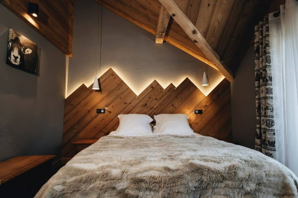 A cozy bedroom with a wooden ceiling, a bed with a fluffy blanket, and a wall-mounted light fixture.