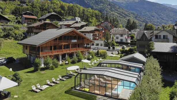 Un complejo turístico de montaña con edificios de estilo chalete, una zona de piscina y un paisaje montañoso de fondo.