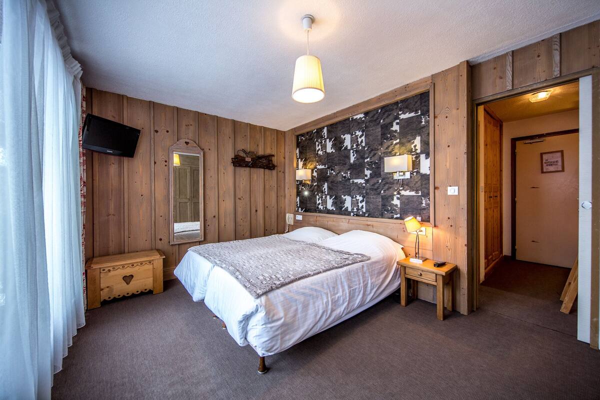 A bedroom with a bed, a nightstand, a mirror, a TV, and a wall with a cow print pattern.