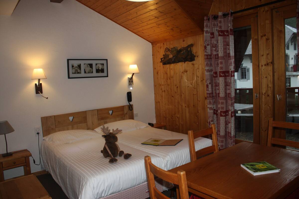 A wooden bedroom with a bed, two bedside lamps, a wall-mounted picture, and a wooden table with a book.
