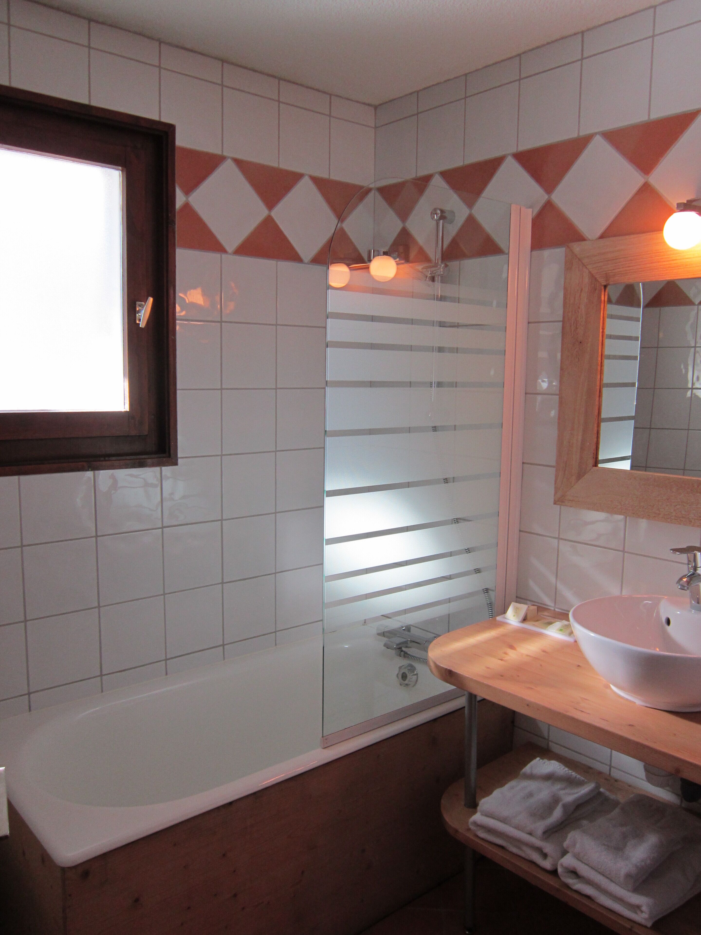 A bathroom with a bathtub, a glass shower enclosure, a sink with a mirror above it, and a window.