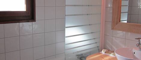 A bathroom with a bathtub, a glass shower enclosure, a sink with a mirror above it, and a window.