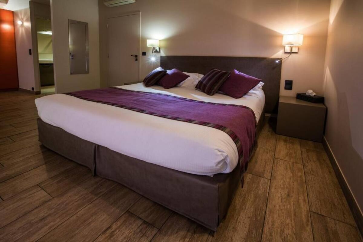 A hotel room with a bed, bedside lamps, a nightstand, and a door.