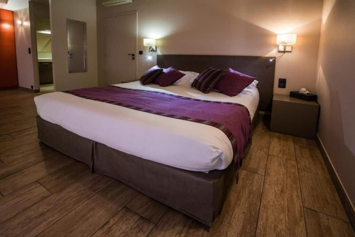 A hotel room with a bed, bedside lamps, a nightstand, and a door.