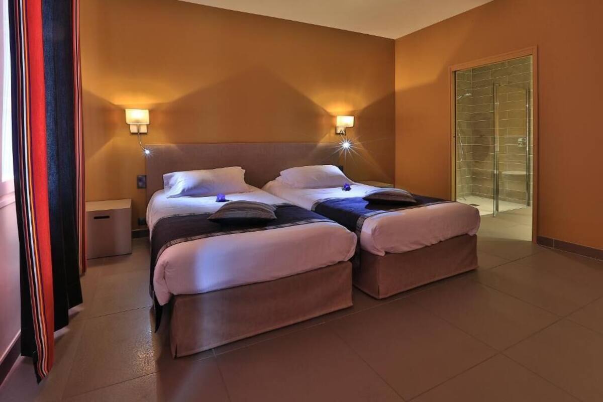 A hotel room with two beds, a nightstand, wall sconces, a sliding glass door, and a red curtain.