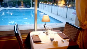Mesa de comedor con lámpara, vasos y cubiertos, con vista a una piscina.